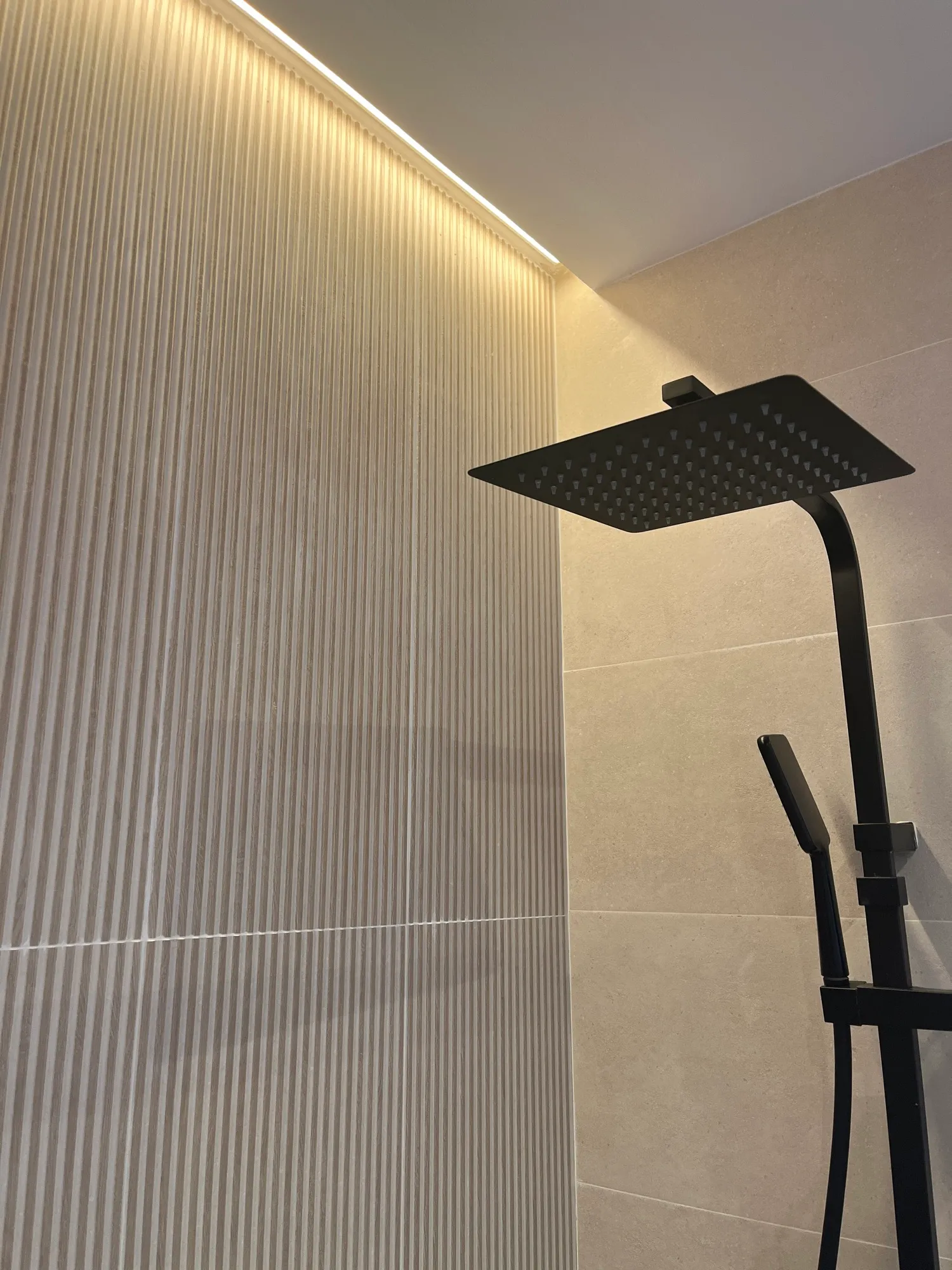 Ducha con rociador negro, pared de relieve acanalado y línea de luz indirecta en el techo