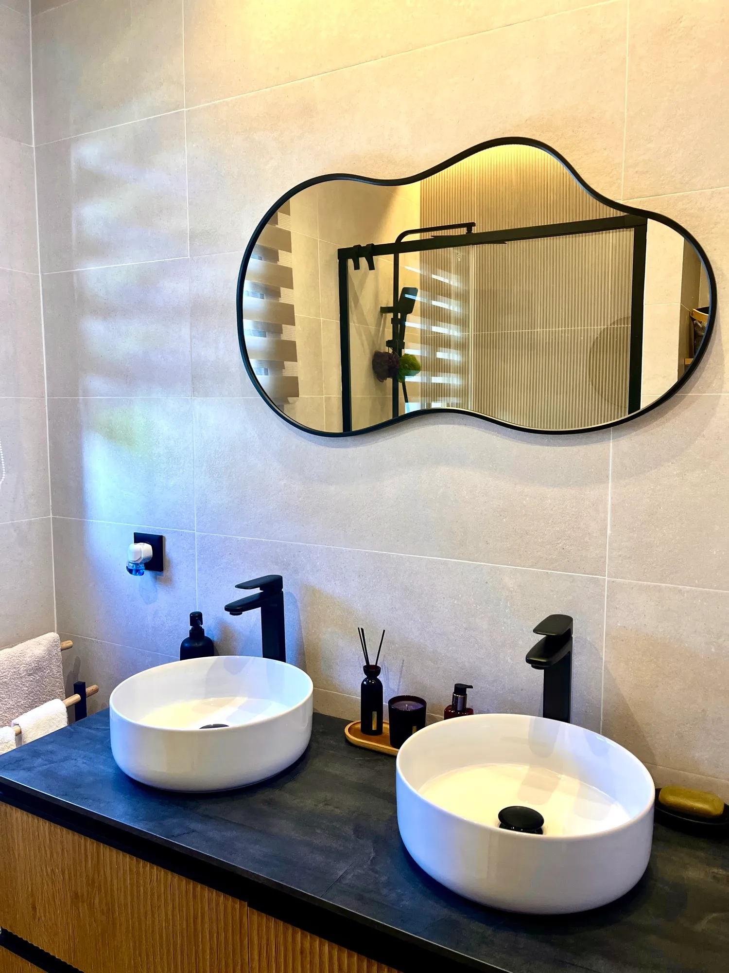 Vista lateral del doble lavabo con mueble de roble ranurado y el espejo reflejando la ducha